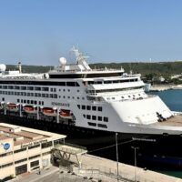 El barco Renaissance, de la naviera francesa ex-CFC (ahora Ambassador Croisières), atracado en una estación marítima con la chimenea morada del antiguo logotipo CFC; al fondo, colinas verdes y aerogeneradores. Foto de Pierre Abel (CC BY-SA 4.0).