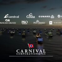 Logotipos de las navieras de Carnival Corporation (AIDA, Carnival, Costa, Cunard, Holland America Line, Princess, P&O y Seabourn) sobre una flota de barcos iluminados en el mar al anochecer. Cortesía de Carnival Corporation.