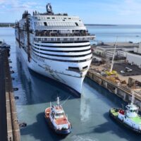 El MSC World Atlantic sale a flote del dique del astillero Chantiers de l'Atlantique, en Saint-Nazaire, con dos remolcadores y las naves del astillero a la derecha. Cortesía de MSC Cruceros.