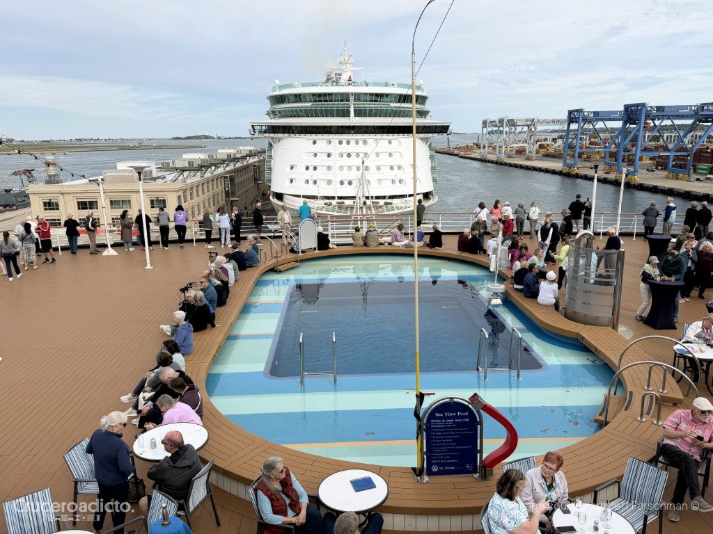 Pasajeros en la Sea View Pool, la piscina de popa del ms Volendam, con el Independence of the Seas al fondo en Boston.