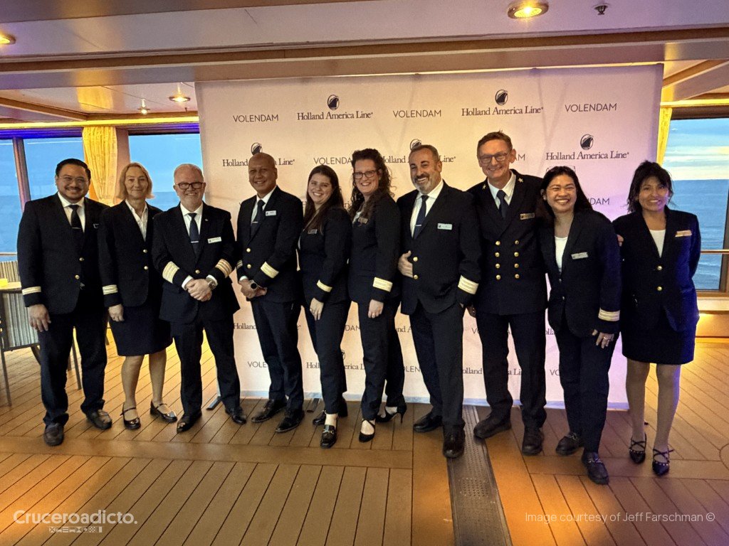 Grupo de oficiales del ms Volendam posando ante un panel con el logotipo de Holland America Line.