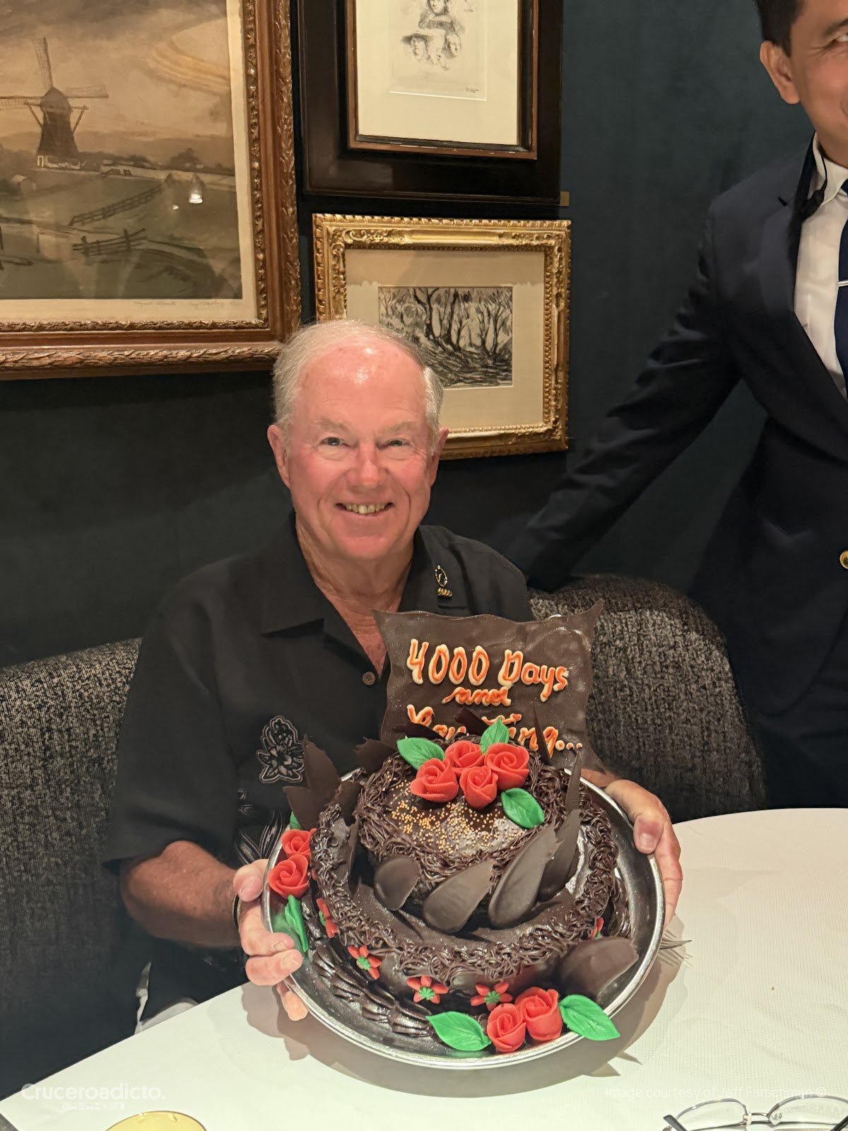 Jeff Farschman sostiene la tarta de chocolate con el cartel de 4.000 días, durante la cena a bordo del ms Volendam.