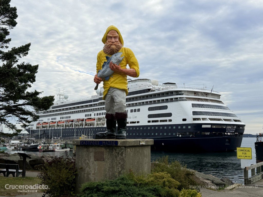 La estatua del pescador de Eastport, con chubasquero amarillo y un pez en la mano, con el ms Volendam al fondo.