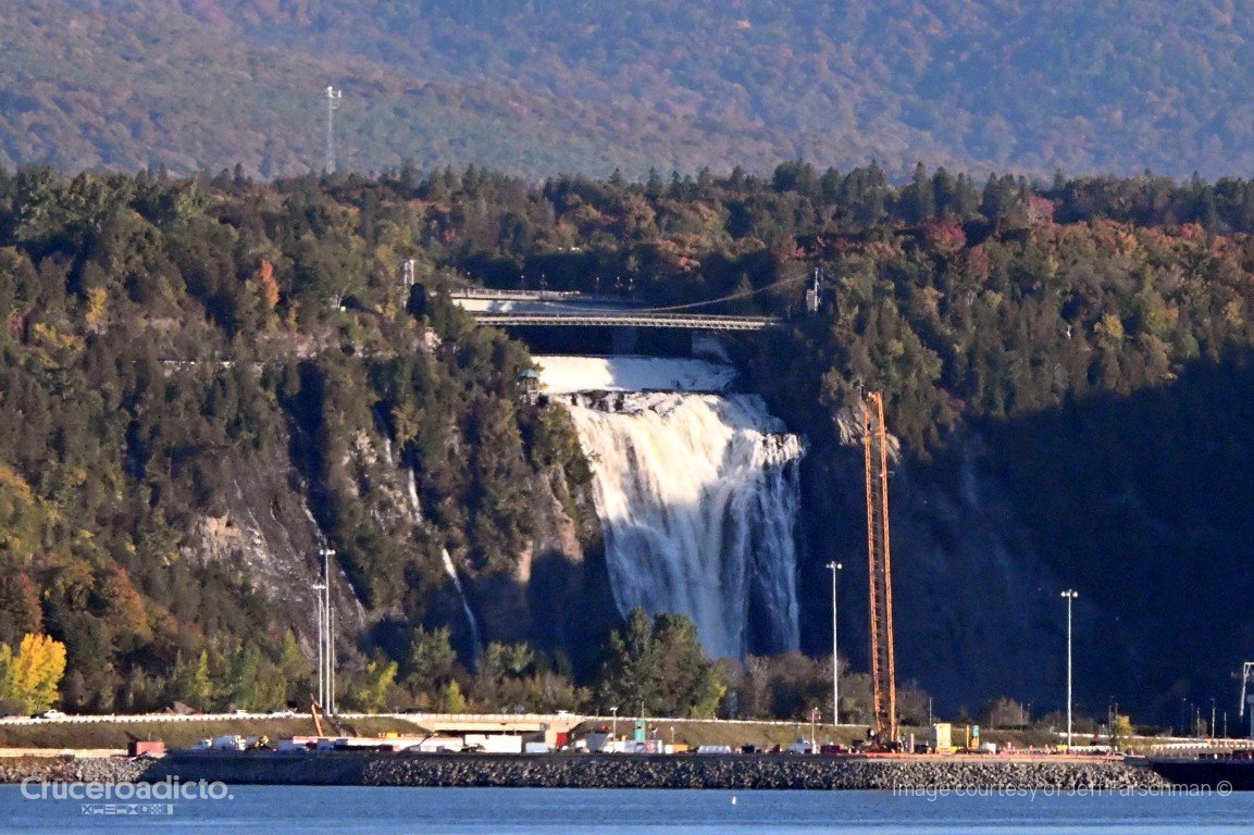 Cascada de gran caída sobre un acantilado boscoso con colores de otoño, cerca de Quebec, vista desde el río.