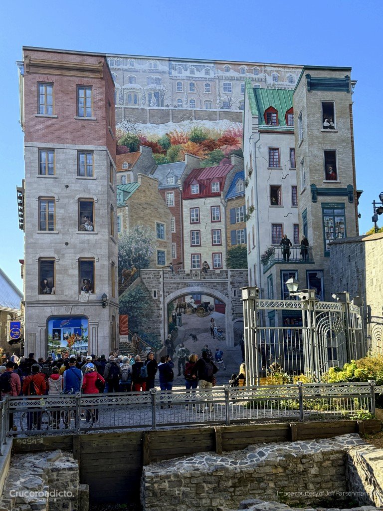 Gran mural en trampantojo que simula edificios y calles de Quebec, con grupos de visitantes delante.