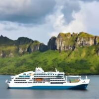 Recreación del Aranoa de Aranui Cruises, con contenedores de carga en la cubierta de proa, navegando frente a una isla montañosa de la Polinesia. Cortesía de Aranui Cruises.
