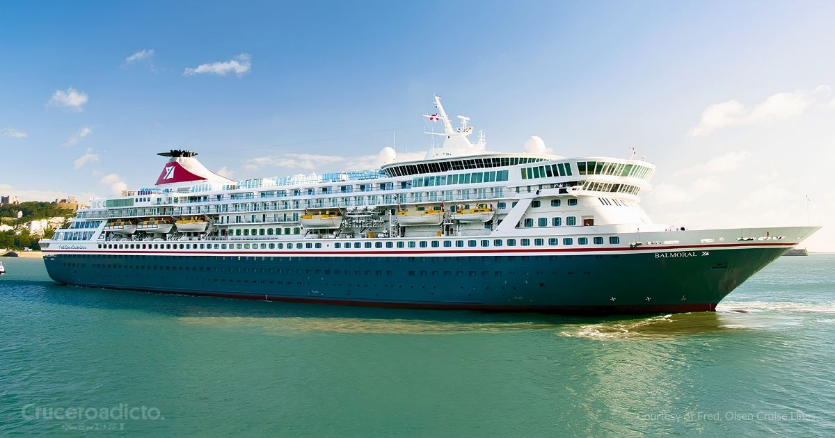 El Balmoral de Fred. Olsen Cruise Lines navegando cerca de la costa, con el casco azul oscuro y la chimenea roja con el logotipo de la naviera. Cortesía de Fred. Olsen Cruise Lines.