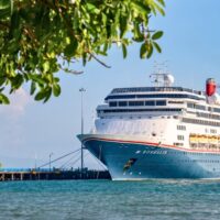 El Borealis de Fred. Olsen Cruise Lines atracado en un muelle de aguas turquesas, con ramas de un árbol en primer plano
