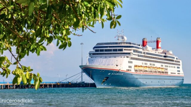 El Borealis de Fred. Olsen Cruise Lines atracado en un muelle de aguas turquesas, con ramas de un árbol en primer plano