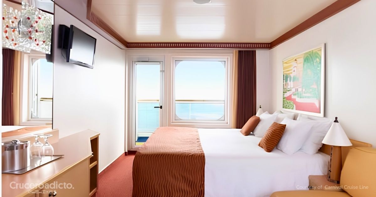 Camarote con balcón de un barco de Carnival Cruise Line, con cama doble, televisor y puerta de cristal abierta al mar. Cortesía de Carnival Cruise Line.