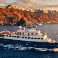 El Callisto de Variety Cruises navegando al atardecer frente a unos acantilados coronados por casas blancas