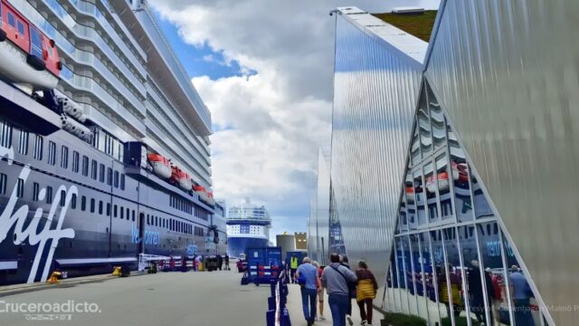 Cruceristas caminando por el muelle de cruceros de Copenhague junto a un barco de Mein Schiff y la terminal de fachada metálica