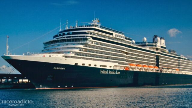 El Eurodam de Holland America Line atracado en un puerto, con su casco azul oscuro y el nombre de la naviera en el costado
