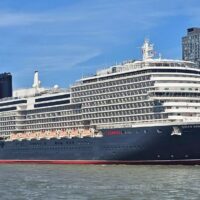 El Queen Anne de Cunard atracado junto a un muelle urbano, con el casco oscuro, el nombre en la proa y la chimenea roja y negra. Imagen de A normal commentor, CC BY-SA 4.0.