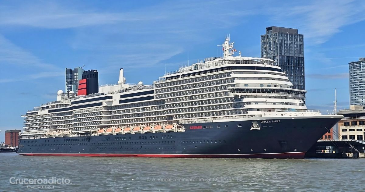 El Queen Anne de Cunard atracado junto a un muelle urbano, con el casco oscuro, el nombre en la proa y la chimenea roja y negra. Imagen de A normal commentor, CC BY-SA 4.0.